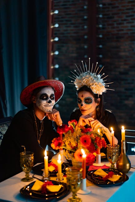 Couple celebrating Dia de los Muertos with traditional makeup and decorations at a dining table.