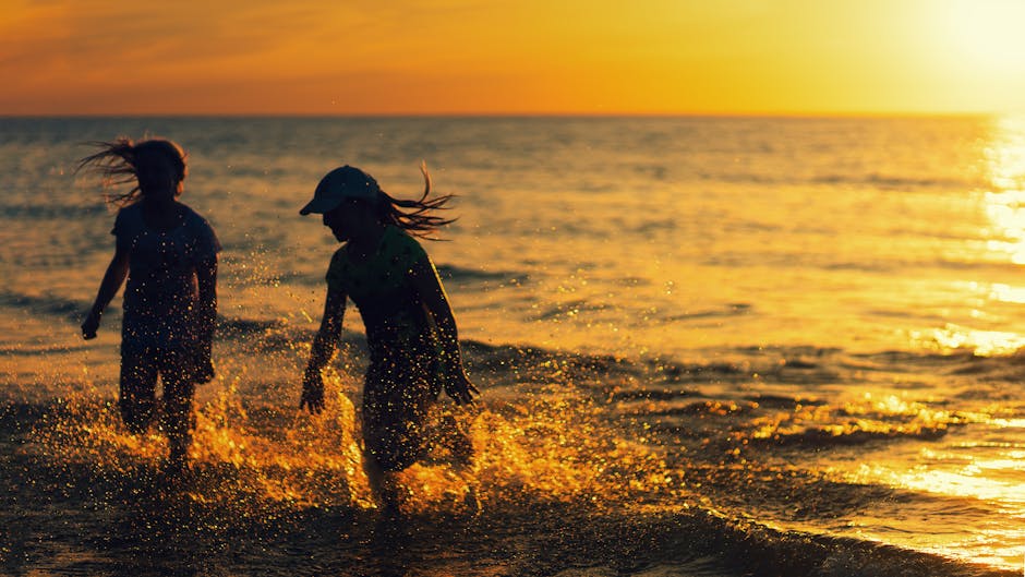 Two children joyfully splash in the water at a beach during sunset, capturing carefree summer fun.